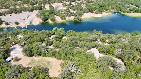 moving above a section of trees that has a tiny cabin campsite near a lake inlet that has a boat ramp and recreational shoreline