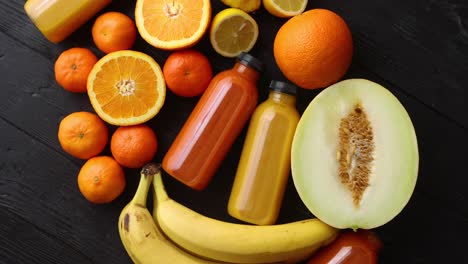 Mix-of-orange-and-yellow-colored-fruits-and-juices-on-black-wooden-background