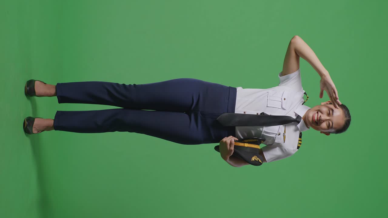 아시아 여성 조종사의 몸이 가득 차 있으며, 녹색 스크린 배경 스튜디오에 서서 경의를 표하고 인사를 하고 있습니다.