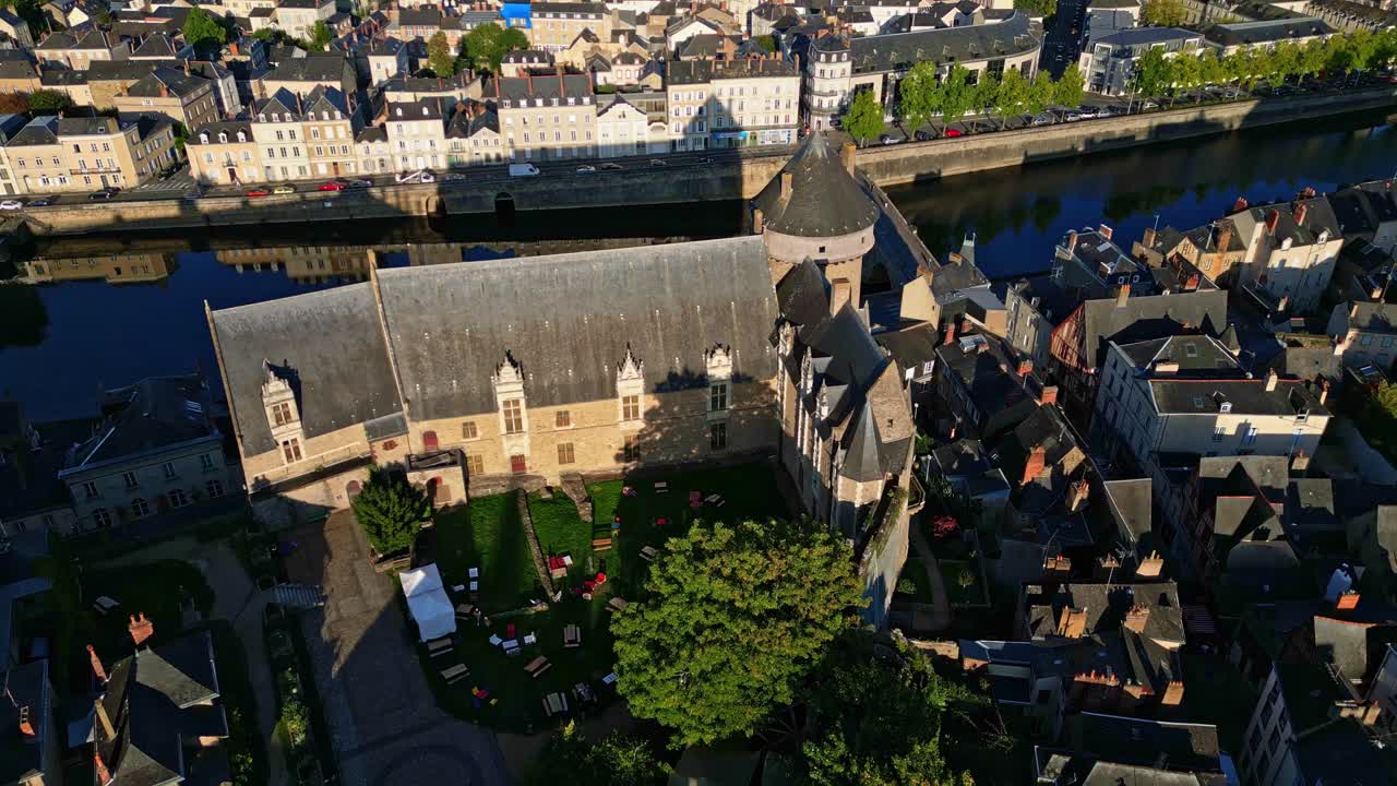 Drone top down view of Château Neuf in Laval showing the courtyard, surrounding houses, vegetation, and the Mayenne River under sunlight