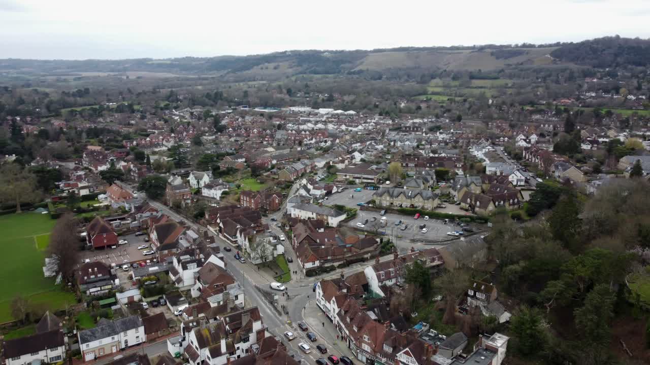 Dynamic parallax aerial footage of Reigate town and Priory Park. Showcasing houses, sports fields, and surrounding greenery under a cloudy sky. A blend of suburban charm and open countryside.