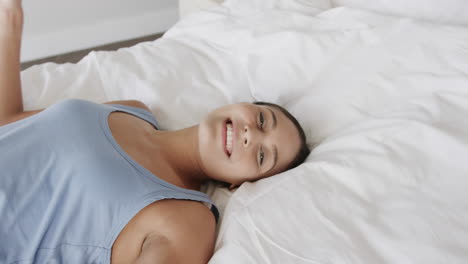 retrato de una mujer biracial feliz acostada en la cama en casa, en cámara lenta