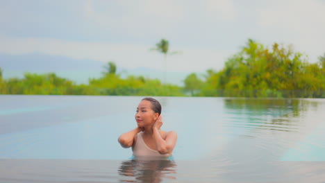 Atractiva-Joven-Toca-Su-Cabello-Mojado-Dentro-Del-Agua-De-La-Piscina-De-Un-Hotel-Exótico-De-Bali-Con-Los-Ojos-Cerrados-En-Un-Día-Soleado,-Retrato-A-Cámara-Lenta