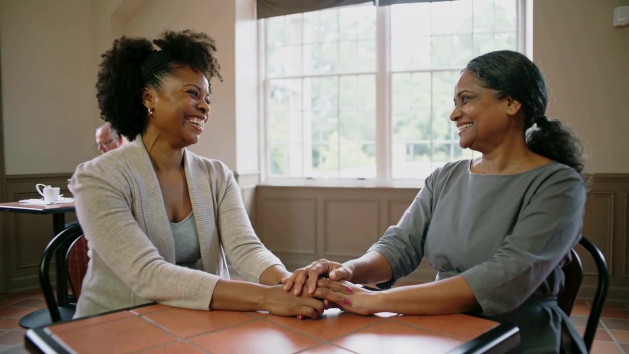 Leaning daughter cardigan starting hand clasp, mother gray top smiling and caring at dining table