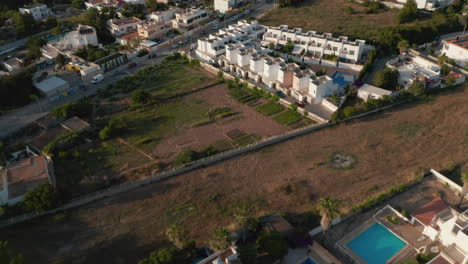 Aerial-shot-of-single-villas-with-swimming-pool-outside-home-and-cars-parked-and-moving-on-city-street-in-Ibiza-in-Spain-during-evening