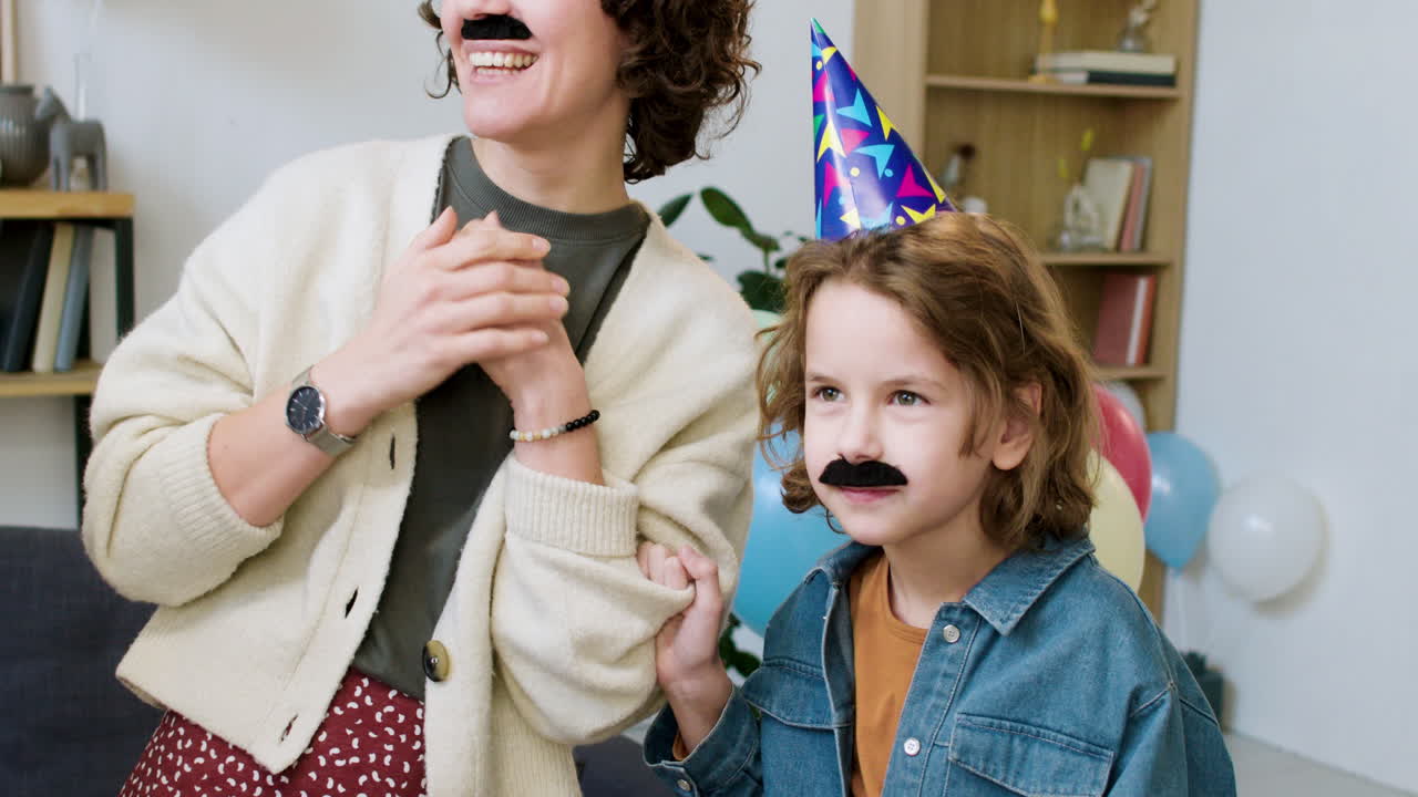 Mother putting moustache on birthday boy's face