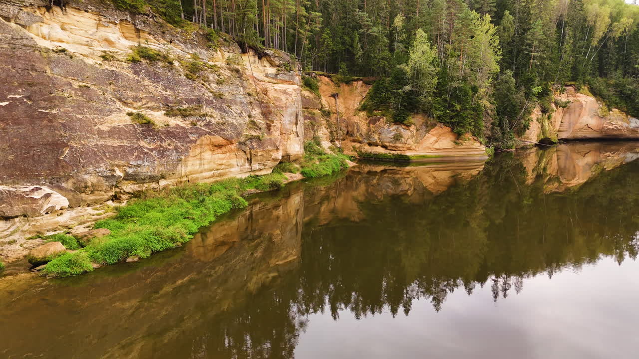 Sandstone cliffs in Gauja National Park reflected in the calm Gauja River in Latvia.