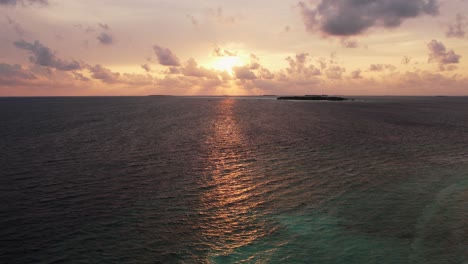 drone view of maldives sunset over calm ocean, panoramic sky and island