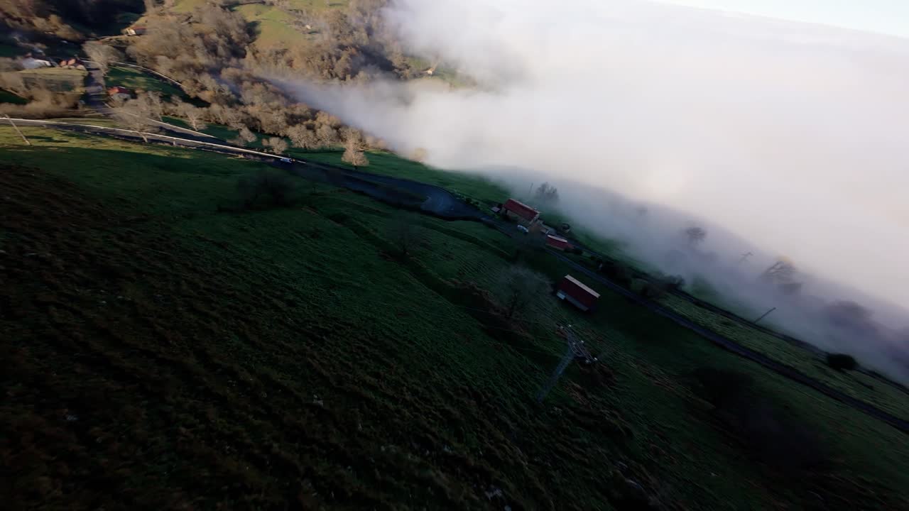 Dynamic FPV shot carving elegant curves through soft morning fog over a green mountain in Cantabria, Spain.