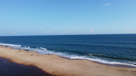 Drone-moving-up-footage-of-varkala-beach,-kerala-during-day-time-and-clear-water-with-blue-sky