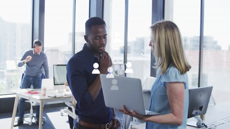 Animation-of-profile-icons-floating-against-diverse-man-and-woman-discussing-over-a-laptop-at-office