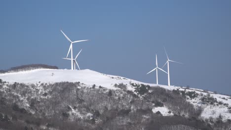 풍력 발전소는 눈 덮인 산, 한국의 하늘 배경에서 볼 수 있습니다.