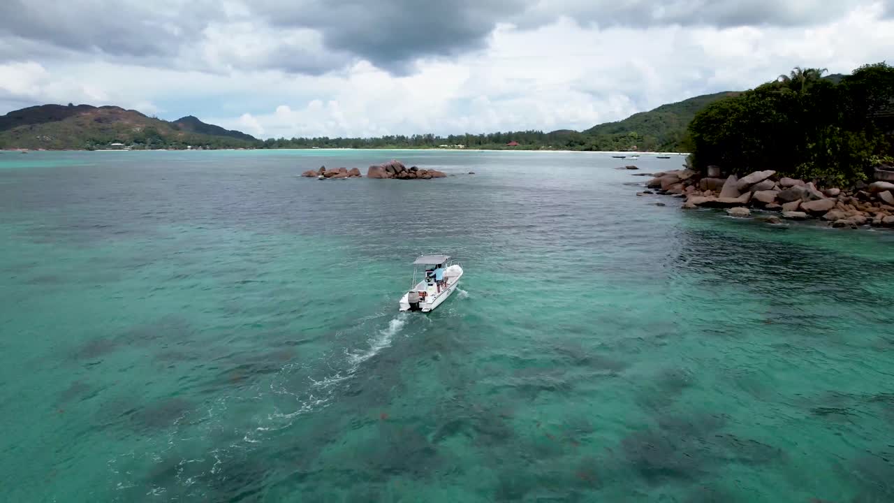 Luchtaanzicht van een witte boot die vaart naar een klein rotsachtig eiland op de Seychellen