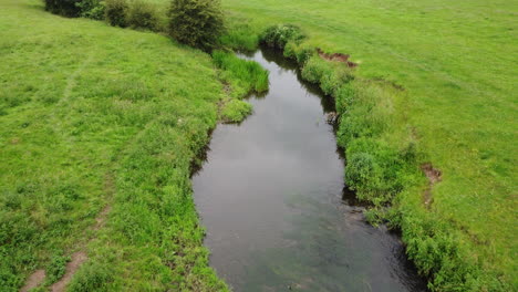 An-aerial-view-of-the-small-river-Arrow-running-through-the-green-fields-of-Warwickshire,-England