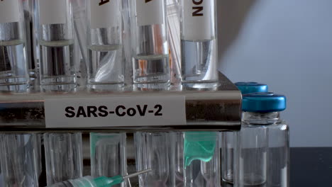 Test-Tubes-Labelled-Alpha-Gamma-Delta-Beta-And-Omicron-Variants-In-Rack-With-Syringes-And-Empty-Vial-Bottles