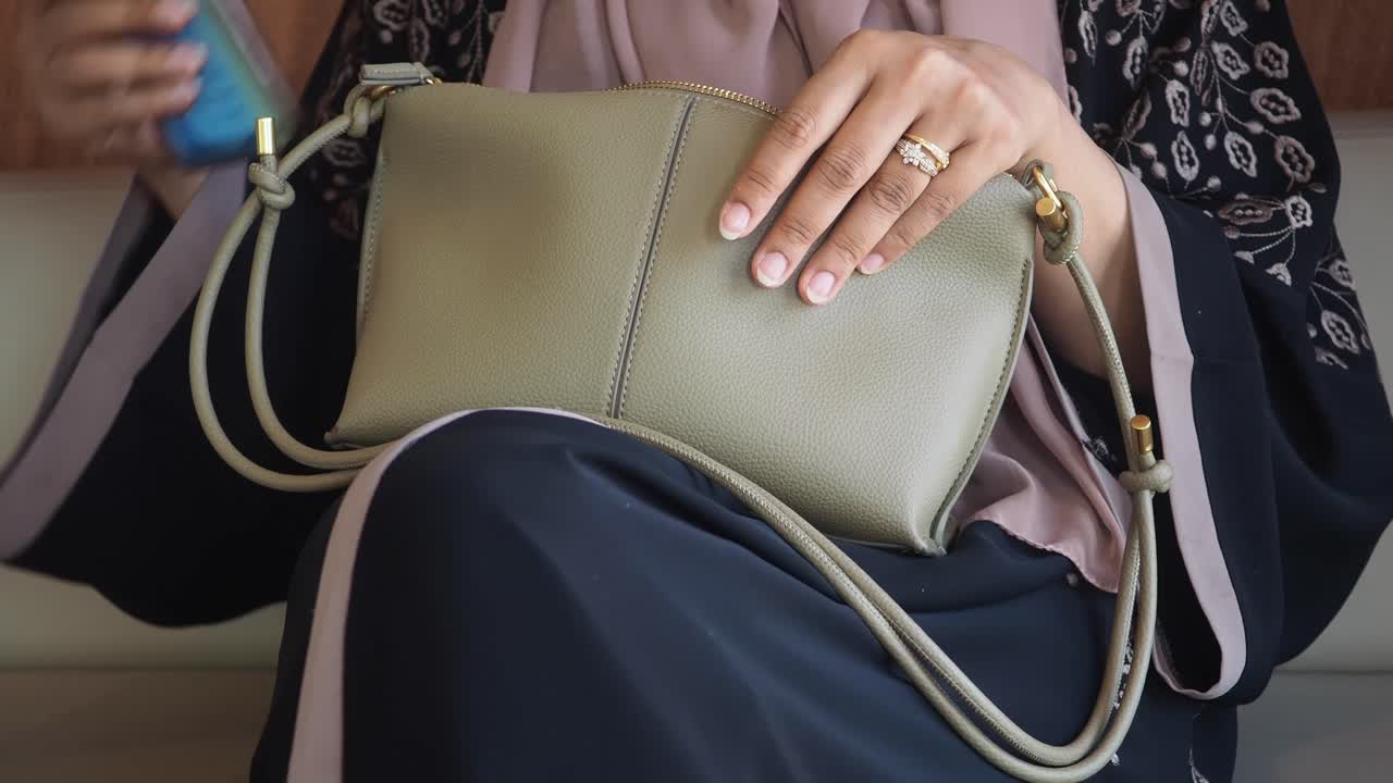 Donna in abaya con una borsa a tracolla grigio chiaro
