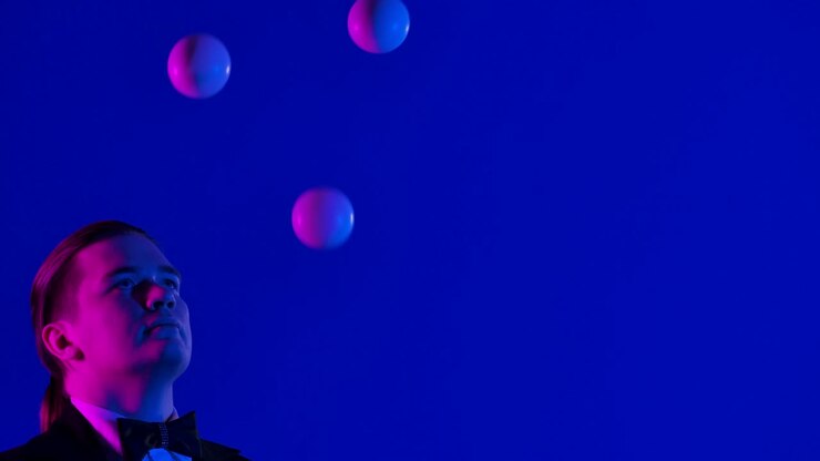 Concentrated juggler uses white balls to juggle. A man demonstrates his professional skills in a dark studio. Blue screen, chroma key. Close up. Slow motion