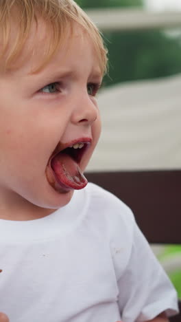 un niño pequeño está sosteniendo un cono de helado, con chocolate manchado en toda su boca, mientras extiende la lengua, cubierto de chocolate