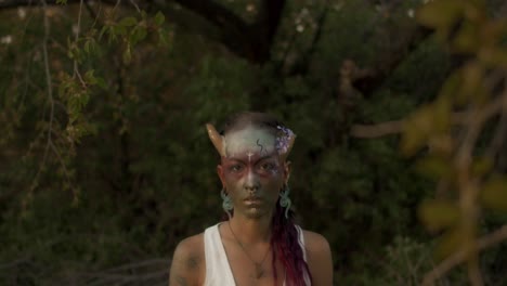 Mystical-Beltane-face-paint-ritual-in-a-forest-at-dusk-as-a-young-attractive-woman-wanders-through-a-dimly-lit-forest-at-twilight,-surrounded-by-lush-greenery-and-a-magical,-hazy-aura