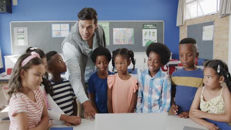 happy diverse male teacher and children using laptop in elementary school class, slow motion