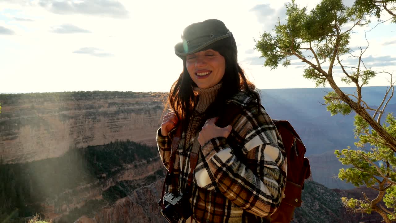 Iloinen naisvaeltaja repun kanssa nauttimassa Grand Canyonin näkymästä auringonlaskun aikaan