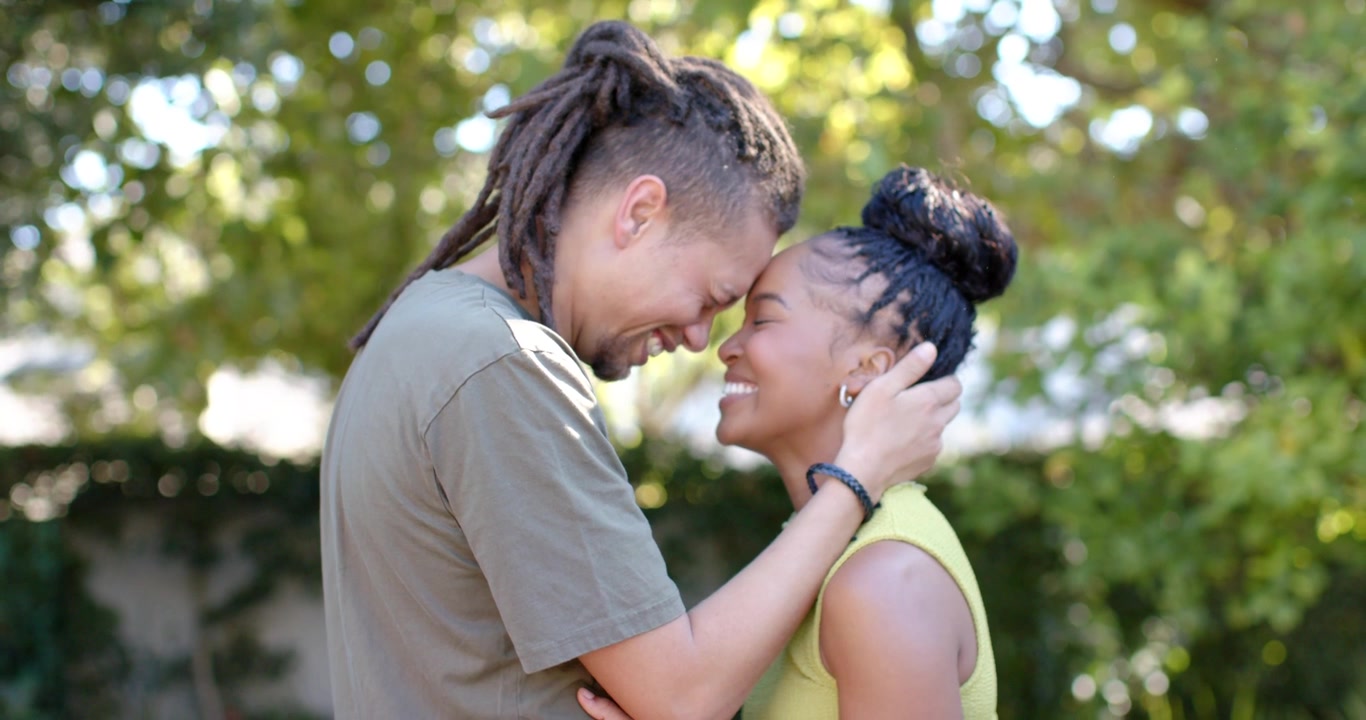African American couple making eye contact, smiling, man tucking hair, cupping face, backyard watch