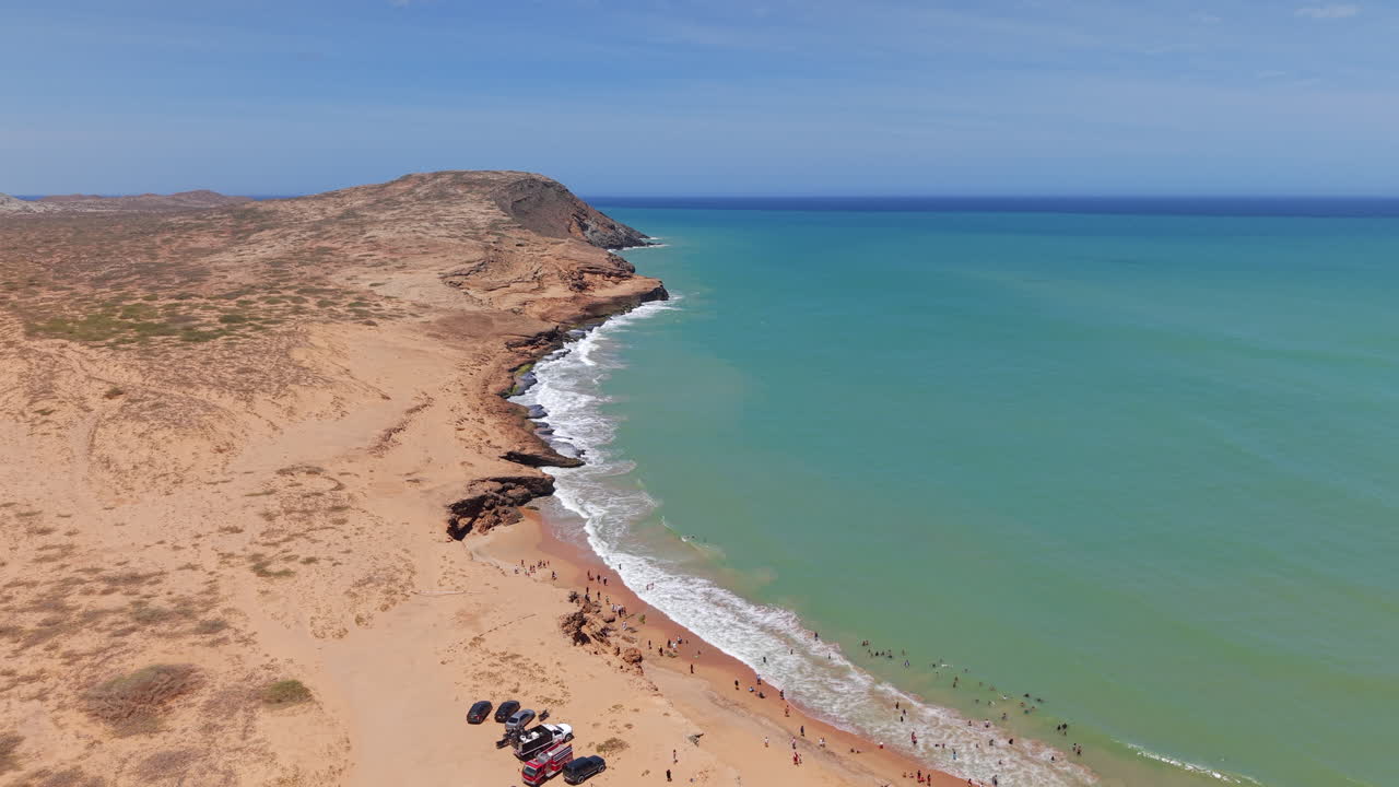 Video drone che riprende la splendida e aspra costa di Playa Dorada, La Guajira, Colombia. Acque cristalline incontrano sabbie dorate sotto un cielo azzurro brillante, offrendo un paesaggio marino tranquillo.