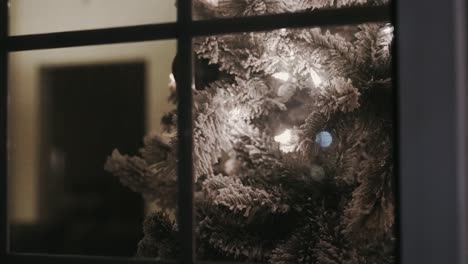 looking in on a close up of a christmas tree from outside the window of a home