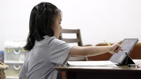 Asian-little-Elementary-school-girl-student-is-taking-online-lessons-during-the-covid-19-epidemic-at-home-in-Bangkok,-Thailand