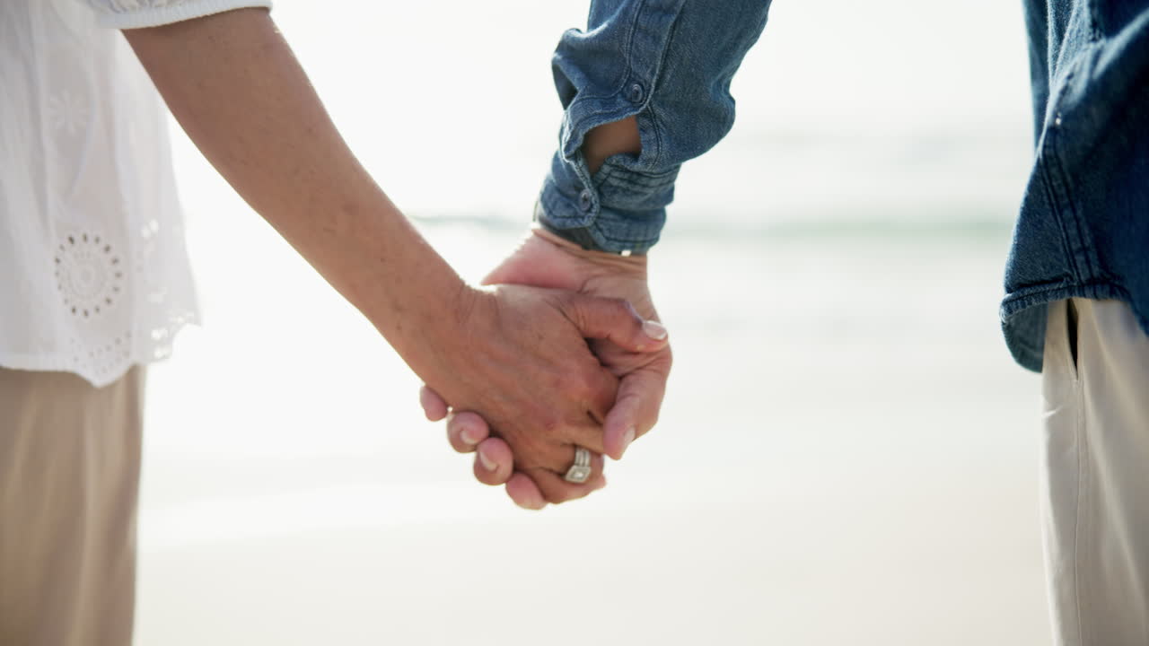 una pareja de mayores tomándose de la mano en la playa.