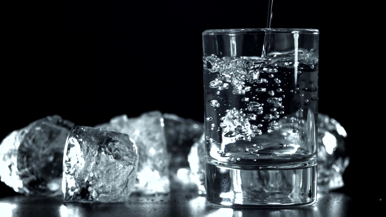 Acqua rinfrescante versata in un bicchiere con cubetti di ghiaccio
