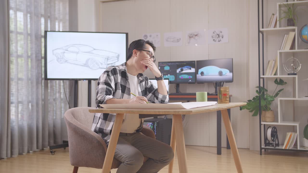 tv와 컴퓨터 디스플레이 3d 전기 자동차 모델과 함께 스튜디오에서 테이블에 자동차 디자인 스케치를 작업하는 동안 아시아 남성 yawn
