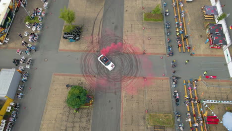 vista aérea de un coche deportivo a la deriva en círculo con humo rojo y huellas de neumáticos