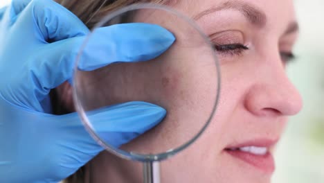 dermatologist examining woman's skin with magnifying glass