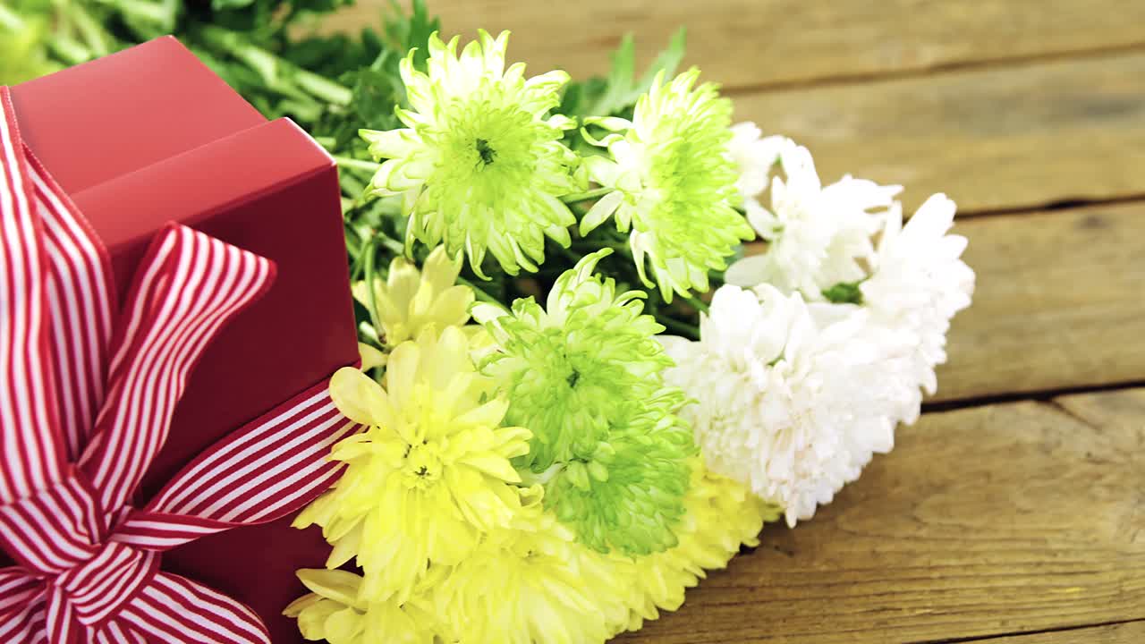 caja de regalos y un ramo de flores amarillas en una tabla de madera