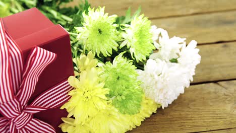 Gift-box-and-bunch-of-yellow-flowers-on-wooden-plank