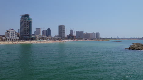 slow cruise over the mediterranean sea near the breakwaters on the beaches of tel aviv, israel with lots of people resting under white umbrellas