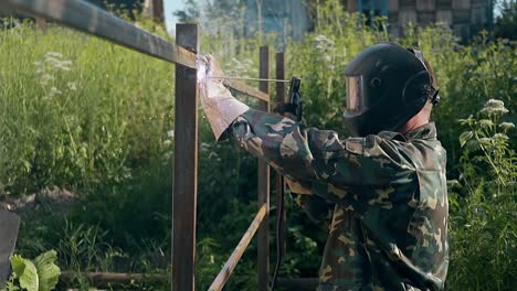 slow-motion-side-view-handyman-in-mask-welds-metal-fence