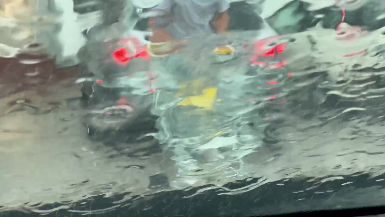 Close up of water droplets on a glass surface with blurred city traffic and car tail lights in the background. Cinematic rainy day atmosphere.