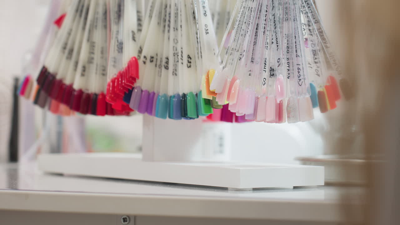 Close up view of vibrant nail polish samples arranged on transparent sticks hanging in salon, showcasing wide variety of colors including red, pink, blue, green, and nude shades under soft lighting