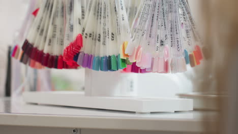 close up view of vibrant nail polish samples arranged on transparent sticks hanging in salon, showcasing wide variety of colors including red, pink, blue, green, and nude shades under soft lighting