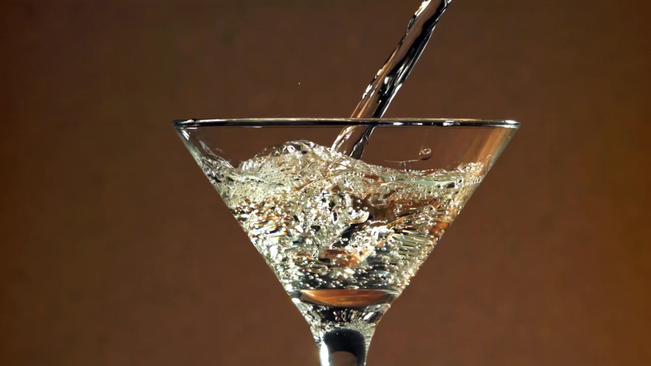 Liquido trasparente versato in un bicchiere da Martini al rallentatore.