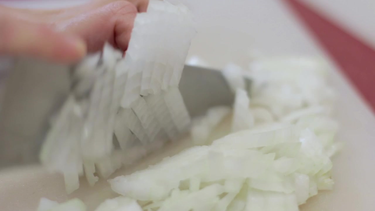 Close up, macro shot of caucasian cook, skilfully chopping up tear inducing onions on a cutting board with a kitchen knife.