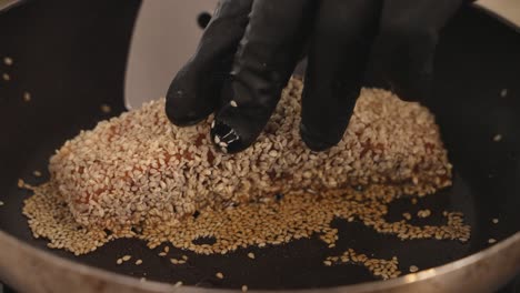 close up shot of a thick cut salmon covered in white sesame seeds sizzling on saute pan, chef using a slotted turner to flip the side, searing in high heat to cook delicious brown crust tataki