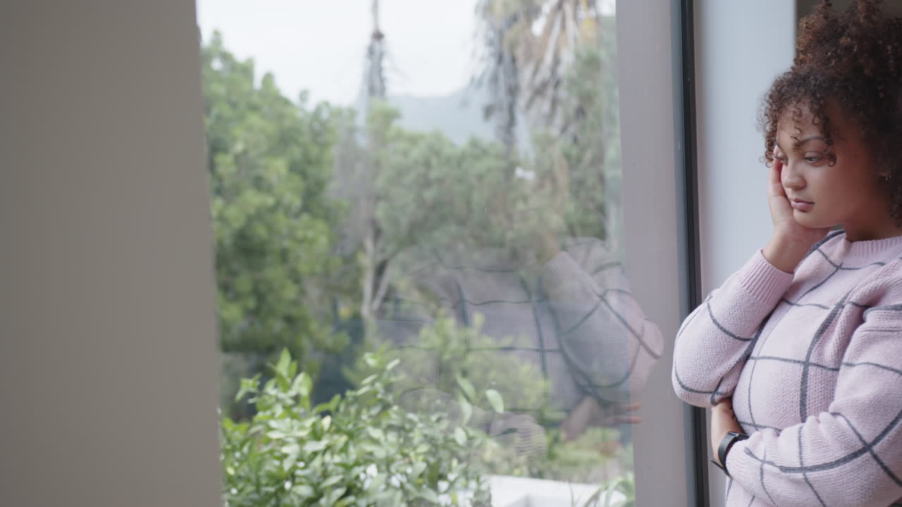 Looking out window, plus size woman in fitness attire relaxing indoors, copy space