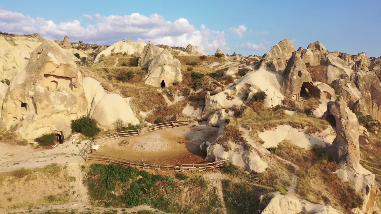 Berrak mavi bir gökyüzünün altında, Güllüdere Vadisi, Kapadokya, Nevşehir, Türkiye'deki beyaz kaya oluşumlarının, konik peri bacalarının ve düz tepeli tüf dağlarının panoramik havadan drone görüntüsü.