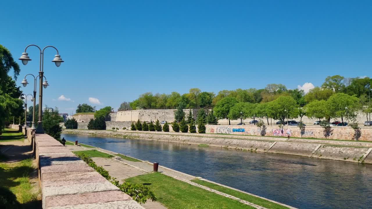Wide view of the Nišava River and the riverside promenade in Niš, Serbia, on a sunny spring day, with clear blue skies and a relaxed atmosphere along the water