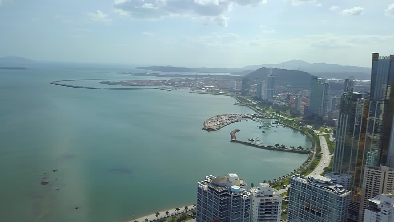 toma aérea de helipuerto, carretera costera cinta costera con puerto - horizonte de rascacielos de gran altura - cerro ancón y canal de panamá en el fondo