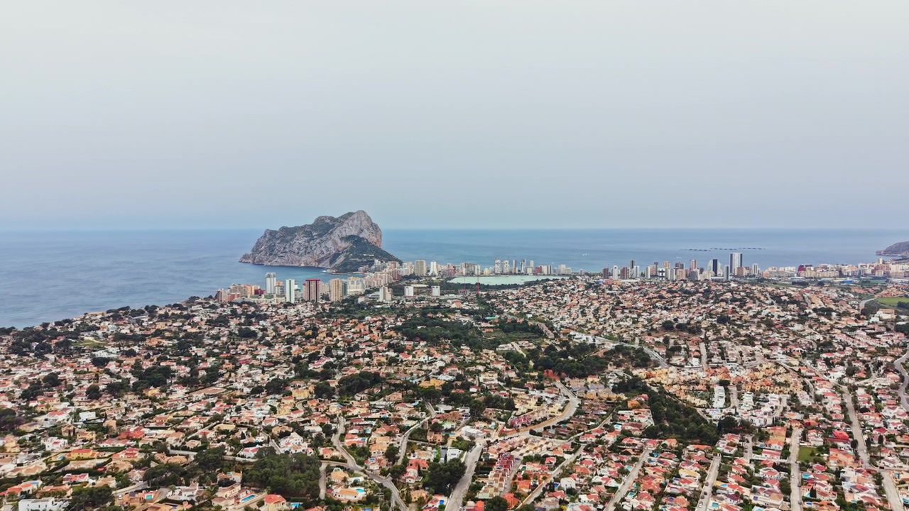 Vista di città costiera con edifici, spiagge e formazione rocciosa in lontananza in una giornata limpida.