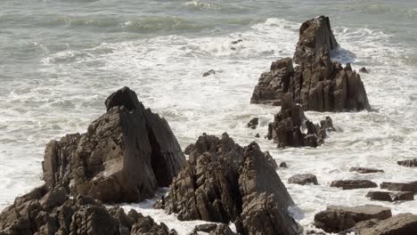 mid-shot-of-waves-crashing-into-jagged-rocks-in-the-Cornish-sea-at-Hartland-Quay,-Stoke,-Hartland,-Bideford